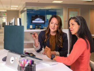 two women sitting at a table looking at a computer screen