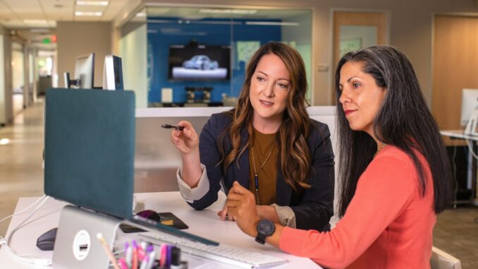 two women sitting at a table looking at a computer screen