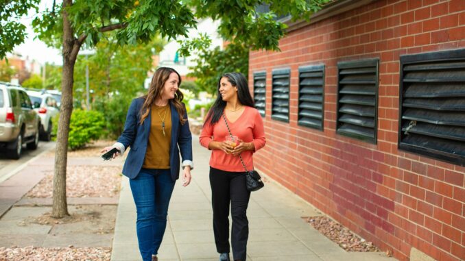 two women walking down a sidewalk talking to each other