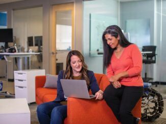 two women sitting on a couch looking at a laptop