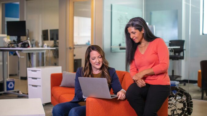 two women sitting on a couch looking at a laptop