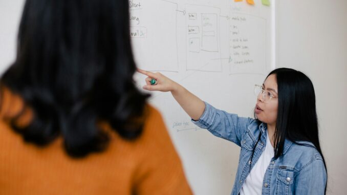 two women standing in front of white dry erase board