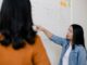 two women standing in front of white dry erase board